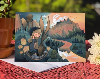 May include: A greeting card featuring a cartoon illustration of a person with a brown rabbit in a mountainous landscape. The person is wearing a blue hat and a blue shirt. The rabbit is brown with long ears. The background is a blue and orange sky with mountains and trees.