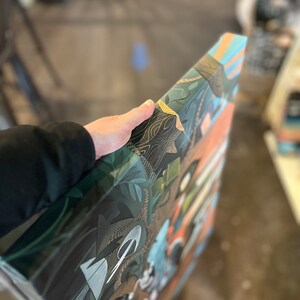 Pu&ograve; includere: Una stampa su tela con un design astratto colorato che presenta una variet&agrave; di forme e motivi. Il design include sfumature di verde, blu, arancione e giallo. La stampa &egrave; incorniciata da un bordo nero.