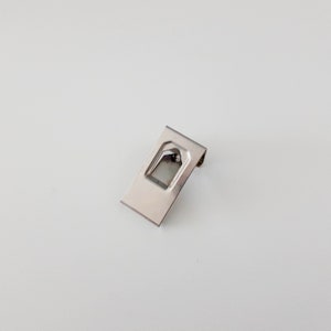 May include: A silver metal bracket with a rectangular shape and a small opening in the center.