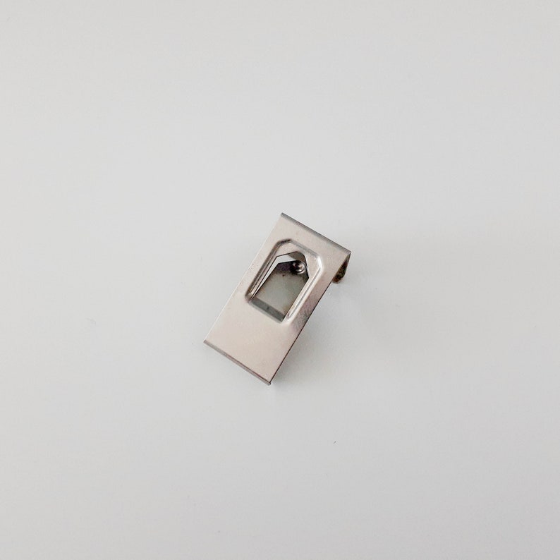 May include: A silver metal bracket with a rectangular shape and a small opening in the center.