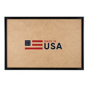 May include: A rectangular framed sign with a brown background and the text "MADE IN USA" in navy blue. The American flag is depicted in red and blue on the left side of the sign. The frame is black.