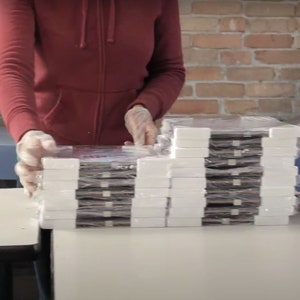 May include: A stack of wrapped books or journals, likely for sale or distribution. The books are wrapped in white paper and have a dark brown cover. The books are stacked on a white table.