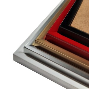 May include: Close-up of the corner of three picture frames, stacked on top of each other. The top frame is black, the middle frame is red, and the bottom frame is silver.