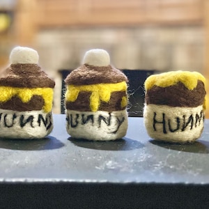 May include: Three small felt jars with yellow honey and the word "HUNNY" written on the front.