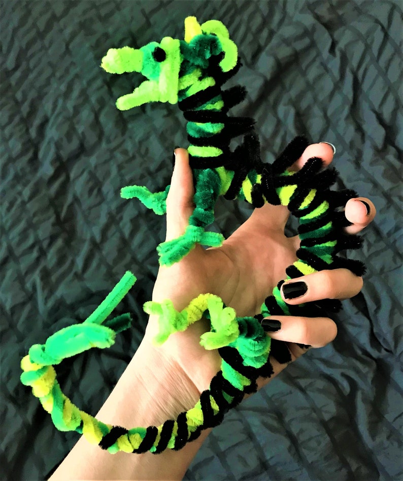 May include: A green and black pipe cleaner dragon with a long tail and a small head. The dragon is made of pipe cleaners that are twisted together to create a 3D shape.
