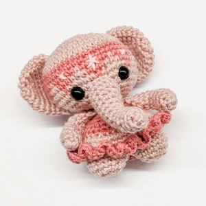 May include: A pink crocheted elephant wearing a pink and white crocheted dress with a ruffled hem.