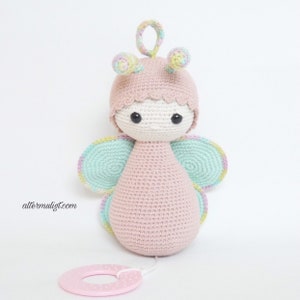 May include: A pink crocheted butterfly toy with green wings and a pink and white rattle. The toy has a white face with black eyes and a pink crocheted hat.