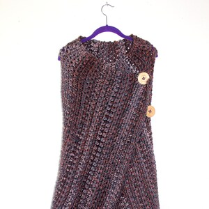 May include: A brown and gray crocheted shawl with two wooden buttons. The shawl is hanging on a purple hanger.