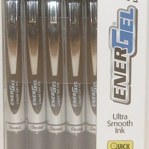 Puede incluir: Un paquete de seis bolígrafos de gel líquido Pentel EnerGel RTX de color negro con una punta mediana de 0,7 mm. Los bolígrafos tienen un acabado plateado y el embalaje dice "Ultra Smooth Ink" y "Quick Drying Great for Lefties".