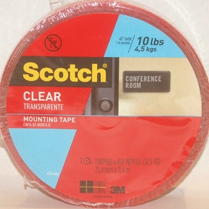May include: A roll of clear Scotch mounting tape with a red label. The label says "Scotch", "Clear", "Transparente", "Mounting Tape", "Cinta de Montaje", "Conference Room", "40" holds 10 lbs 4,5 kgs", "1 IN/PULG x 450 IN/PULG (12.5 YD)", "25,4 mm x 11,4 m", and "3M".