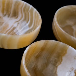 K&ouml;nnte beinhalten: Drei dekorative Schalen aus durchscheinendem, geb&auml;ndertem Onyx. Die Schalen haben eine abgerundete Form mit einer glatten, polierten Oberfl&auml;che. Die Farbe ist eine Mischung aus cremewei&szlig; und goldgelb mit wirbelnden Mustern.