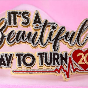 Peut inclure: Décoration de gâteau dorée, noire et argentée avec le texte "IT'S A Beautiful DAY TO TURN 20". Le chiffre 20 est à l'intérieur d'un cœur rouge avec une ligne de battement de cœur rouge.