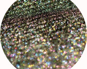 May include: Close-up of a circular image filled with iridescent glitter. The glitter particles are a mix of colors, including silver, gold, green, and pink, creating a shimmering effect. The glitter is densely packed, with a gradient from dark to light.