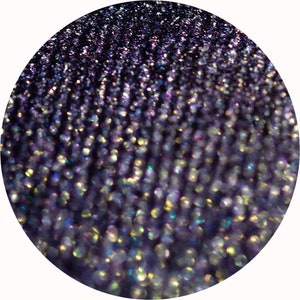 Op de afbeelding: Close-up van een donkerpaarse ondergrond met iriserende glitter. De glitter creëert een glinsterend effect in verschillende kleuren, waaronder goud, blauw en groen.
