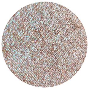 May include: A circular, close-up view of a shimmering, textured surface. The color is a blend of light brown and iridescent hues, with a glittery effect. The texture appears granular, with tiny, reflective particles.