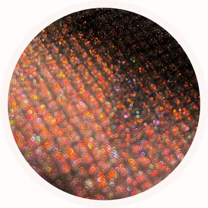 May include: Abstract, circular image with a gradient of colors. The image transitions from dark brown to orange and red, with a scattering of iridescent, bokeh-like circles. The overall effect is glittery and textured.