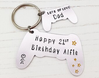 Op de afbeelding: Een zilverkleurige metalen sleutelhanger in de vorm van een gamecontroller. De sleutelhanger heeft de tekst "Happy 21st Birthday Alfie" en "Lots of Love Dad". Het ontwerp bevat een stokfiguur en sterren.