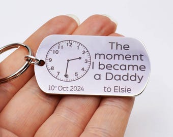 May include: Silver keychain with a clock face and the text "The moment I became a Daddy to Elsie" and the date "10th Oct 2024".