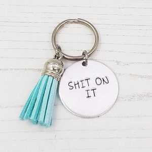 May include: A silver keychain with a turquoise tassel and a round charm that says "SHIT ON IT".