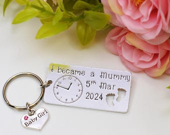 Pode incluir: Chaveiro de prata com um charme em forma de coração que diz "Baby Girl" e uma etiqueta retangular que diz "I became a Mummy 5th Mar 2024" com um relógio e duas pegadas.