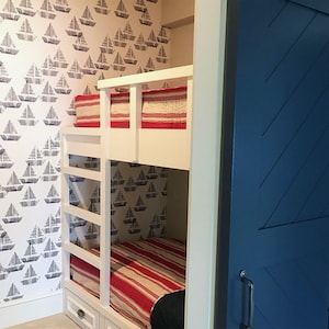 May include: White bunk bed with a red and white striped comforter on the top bunk and a red and white striped comforter on the bottom bunk. The bunk bed is in a room with white walls and a blue door.