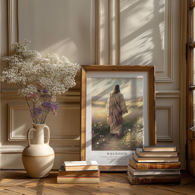 Puede incluir: Una impresi&oacute;n enmarcada que representa a Jes&uacute;s caminando por un campo, con el texto "WALK WITH ME". Un jarr&oacute;n con flores blancas y moradas est&aacute; a la izquierda. Una pila de libros est&aacute; frente al marco.
