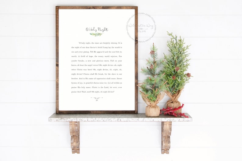 May include: A rectangular framed sign with a dark wood border featuring the text O Holy Night and the lyrics to the Christmas carol printed in black on a white background, accompanied by two small artificial pine trees in burlap bases.