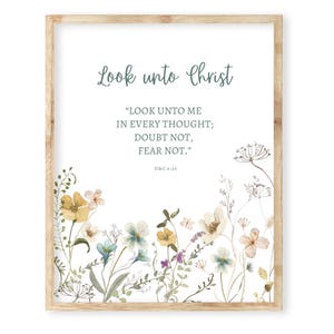 May include: A framed print with a light wood frame. The print features the text "Look unto Christ" in a script font, along with a quote. The bottom of the print is decorated with watercolor flowers in shades of yellow, blue, and purple.