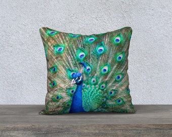 Könnte beinhalten: Ein dekoratives Kissen mit einem leuchtenden Pfau, dessen Schwanzfedern in einer farbenfrohen Darstellung von Grün, Blau und Gold ausgebreitet sind.