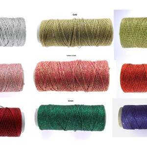 Puede incluir: Una colección de coloridas bobinas de hilo en varios tonos, incluyendo plata, oro, verde lima, rosa, rojo, verde, naranja y morado. Cada bobina está etiquetada con su nombre de color, ofreciendo una amplia gama de opciones para proyectos de manualidades y decoración.