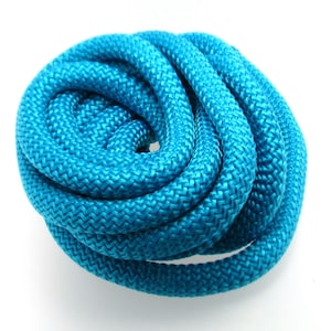 Puede incluir: Un largo de cuerda enrollada de color azul turquesa brillante. La cuerda está hecha de un material suave y tejido, ideal para manualidades u otros proyectos.