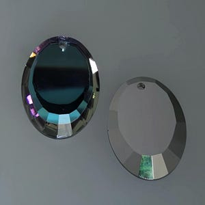 Puede incluir: Dos prismas de cristal redondos con un agujero en la parte superior para colgar. El prisma de la izquierda es iridiscente con un tono azul, morado y verde. El prisma de la derecha es transparente.
