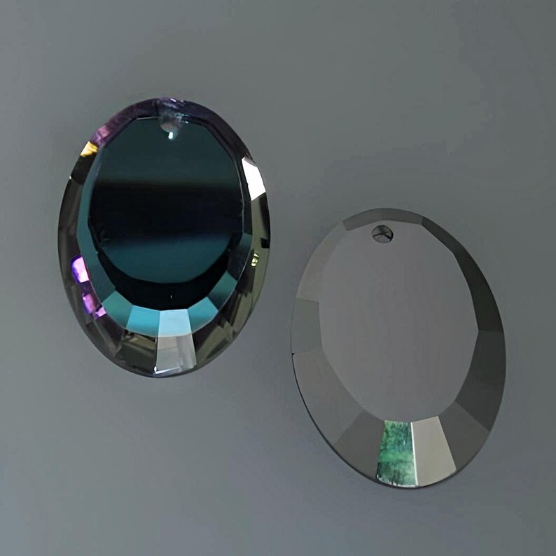 Puede incluir: Dos prismas de cristal redondos con un agujero en la parte superior para colgar. El prisma de la izquierda es iridiscente con un tono azul, morado y verde. El prisma de la derecha es transparente.