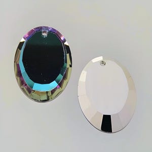 Puede incluir: Dos colgantes de cristal de forma ovalada con un agujero en la parte superior para colgar. Un colgante es transparente y el otro es iridiscente.
