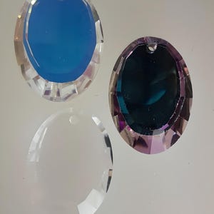 Puede incluir: Tres prismas de cristal de forma ovalada con un agujero en la parte superior para colgar. Los prismas son transparentes, azules y morados.
