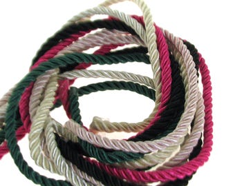 May include: A close-up of a bundle of twisted cord in four colors: black, green, pink, and cream. The cord is arranged in a circular shape.