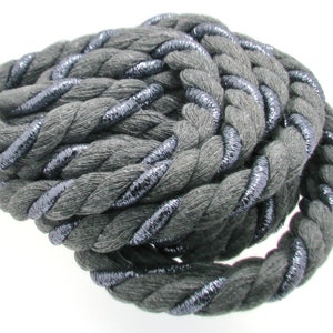 Puede incluir: Cuerda de algodón gris con un hilo metálico plateado que la atraviesa. La cuerda está trenzada y enrollada.