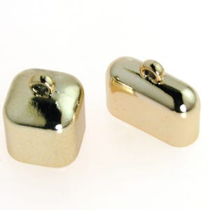 Könnte beinhalten: Zwei goldfarbene Metall-Endkappen für Schnüre oder Bänder. Eine Endkappe ist quadratisch und die andere rechteckig. Beide haben eine kleine Schlaufe oben.