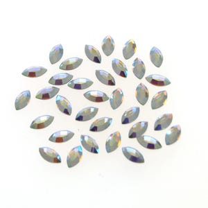 May include: A scattering of iridescent marquise-shaped rhinestones on a white background.