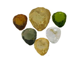 May include: Six faceted glass beads in various colours, including clear, yellow, green, and brown. The beads are shaped like hearts and have a smooth, polished finish.