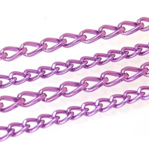 May include: Close-up of several strands of purple metal chain links. The chains are arranged diagonally across a white background, showcasing their glossy, metallic finish. The links are uniform in shape and size.
