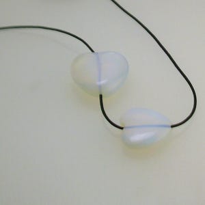 Pode incluir: Um colar com dois pingentes em forma de cora&ccedil;&atilde;o branco em um cord&atilde;o preto.