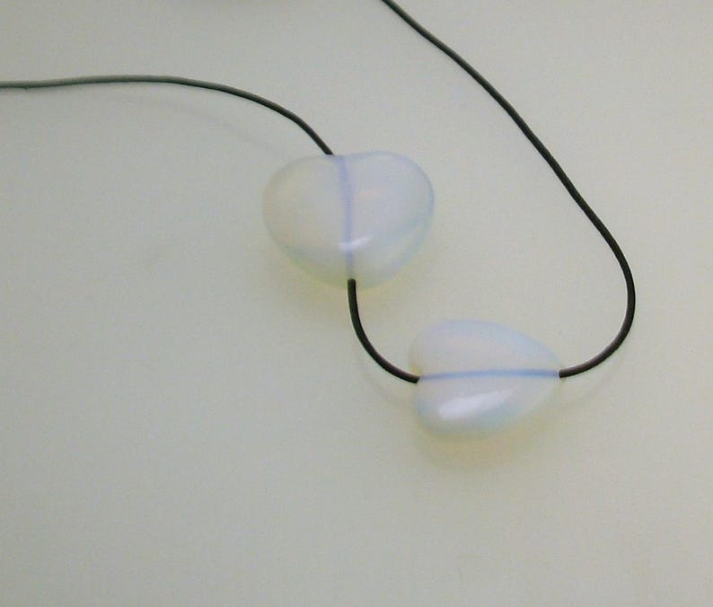 Pode incluir: Um colar com dois pingentes em forma de cora&ccedil;&atilde;o branco em um cord&atilde;o preto.