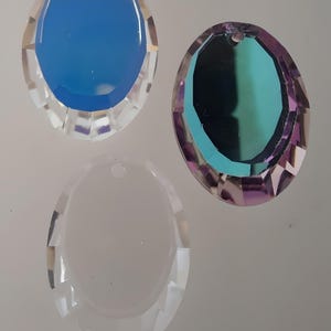 Puede incluir: Tres colgantes de cristal de forma ovalada con bordes facetados. Los colgantes son transparentes, azul claro y verde iridiscente.