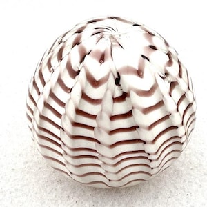 May include: A decorative glass orb with a white base and alternating bands of wavy, dark mauve stripes. The orb has a textured surface and a rounded shape, suitable for home decor.