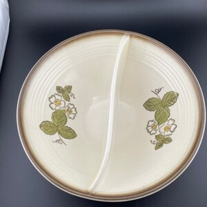 May include: A divided serving dish with a brown rim and a white center. The dish is decorated with a floral pattern of white flowers and green leaves. The flowers are stylized and resemble strawberries.