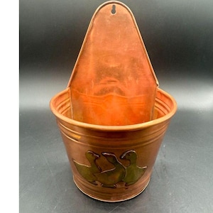 May include: A wall-mounted copper planter featuring a semi-circular basin and a tall, pointed backplate with a pre-drilled hole for hanging. The front of the basin is decorated with a relief design of three geese in a dark, metallic finish.