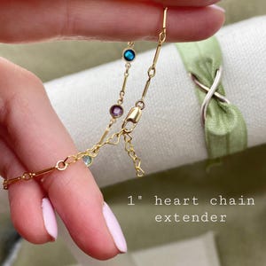 May include: A gold chain with a heart-shaped extender and small colorful gemstones. The chain is 1 inch long and is shown being held by a hand.