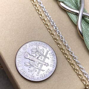 May include: Two gold chains and one silver chain lie on a brown surface next to a US dime. The dime is face up and shows the words "United States of America" and "One Dime".