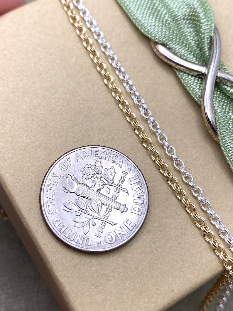 May include: Two gold chains and one silver chain lie on a brown surface next to a US dime. The dime is face up and shows the words "United States of America" and "One Dime".